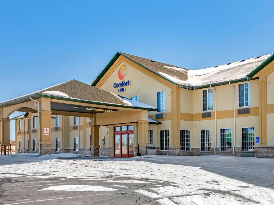 Um hotel Comfort Inn com entrada coberta, várias janelas e estacionamento coberto de neve.