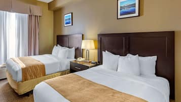 A hotel room with two beds, a nightstand with a lamp, a telephone, and two framed pictures on the wall.