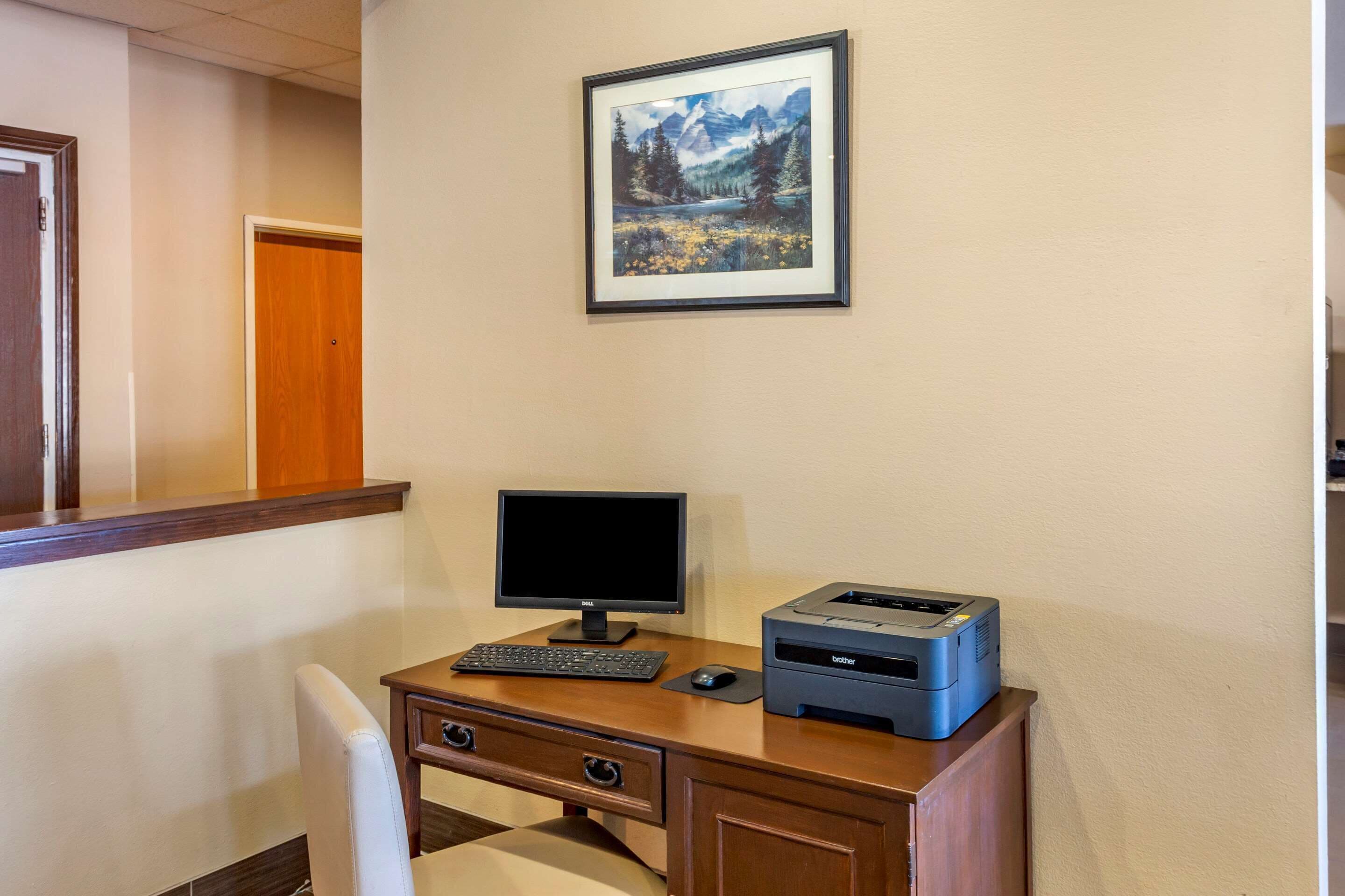 Habitación de hotel con escritorio, computadora, impresora y un cuadro con un paisaje en la pared.