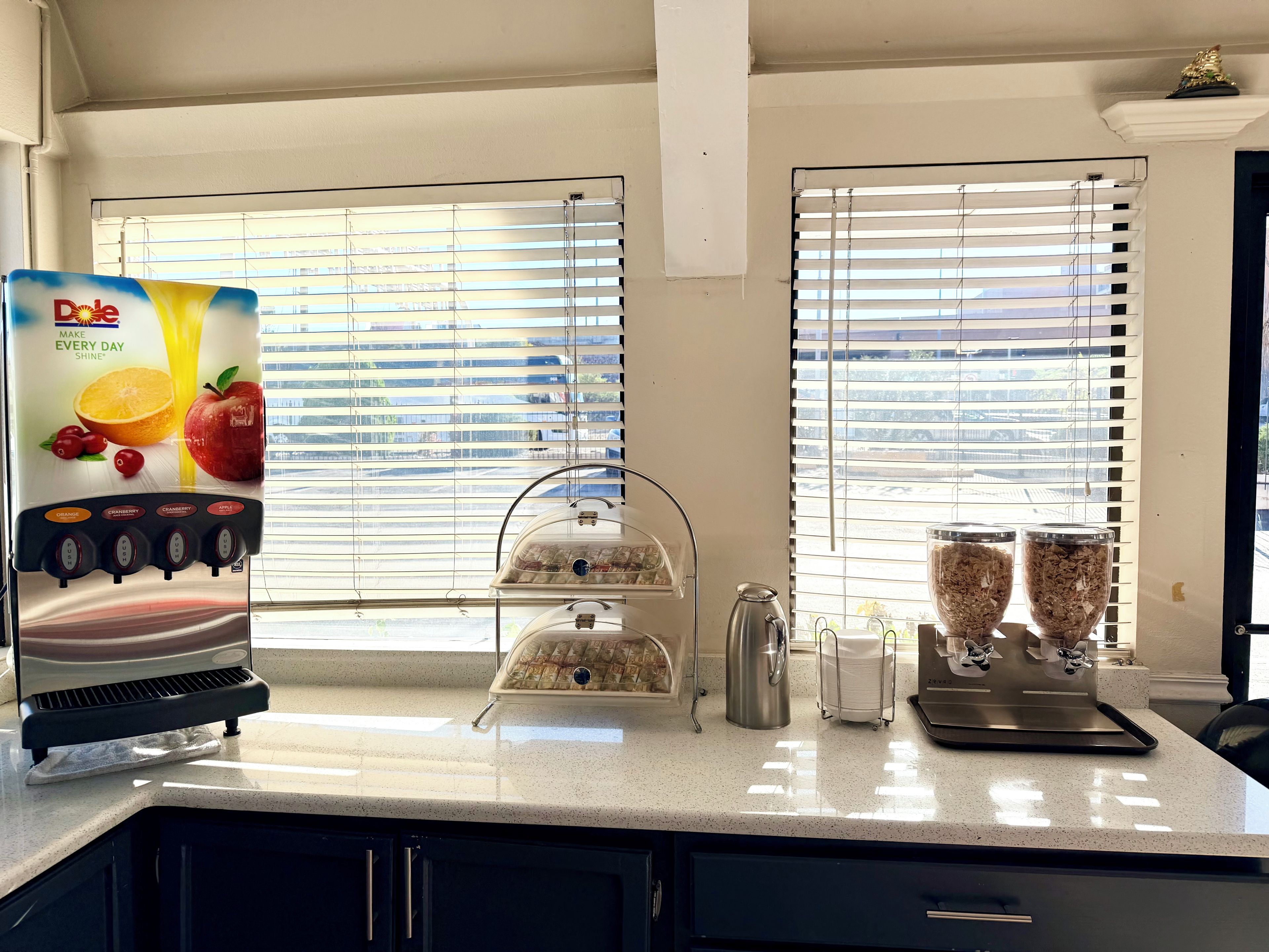 A kitchen with a juice dispenser, a coffee maker, and a food display.