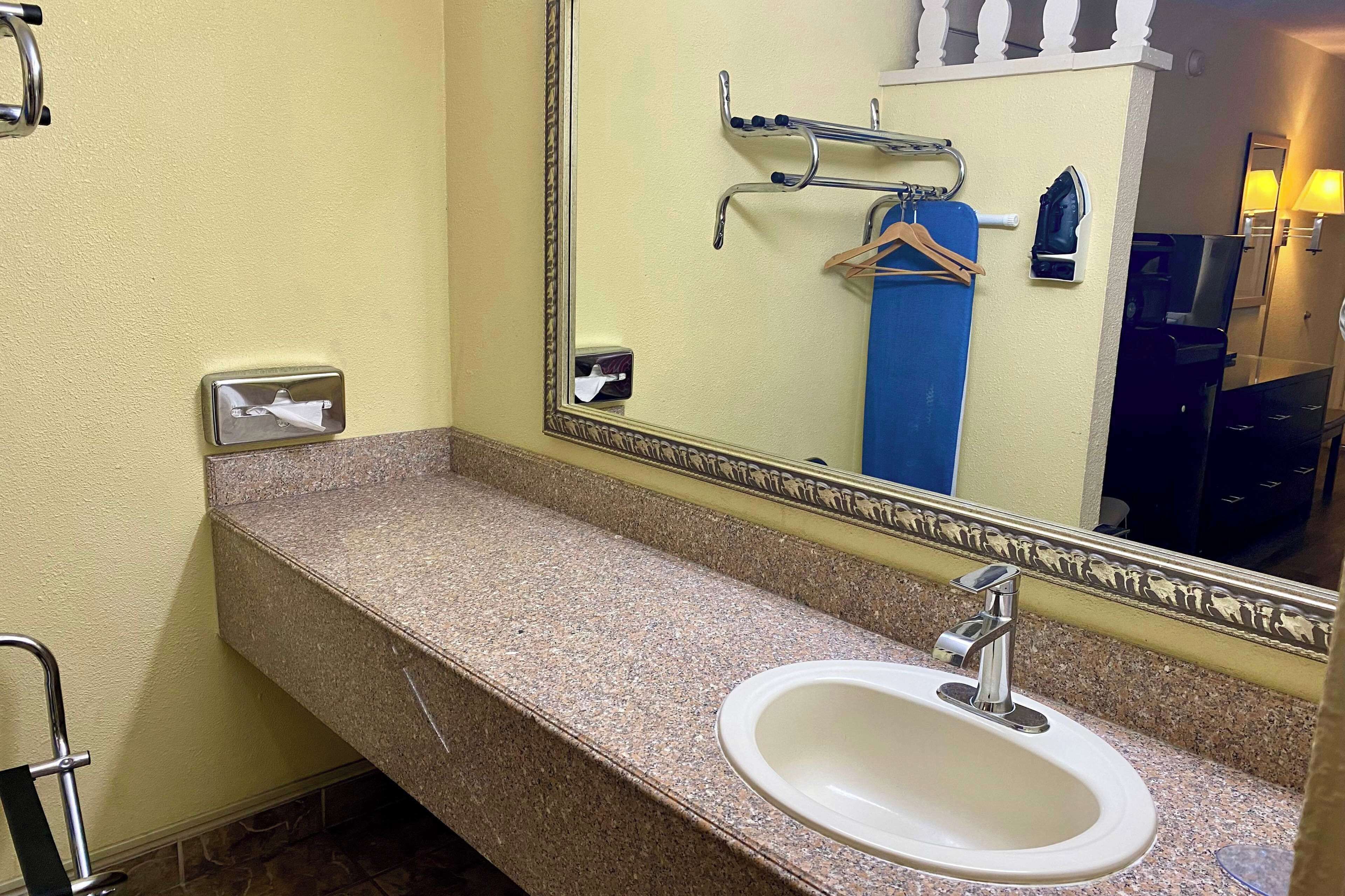 A bathroom with a granite countertop, a white sink, a large mirror, and a towel rack.