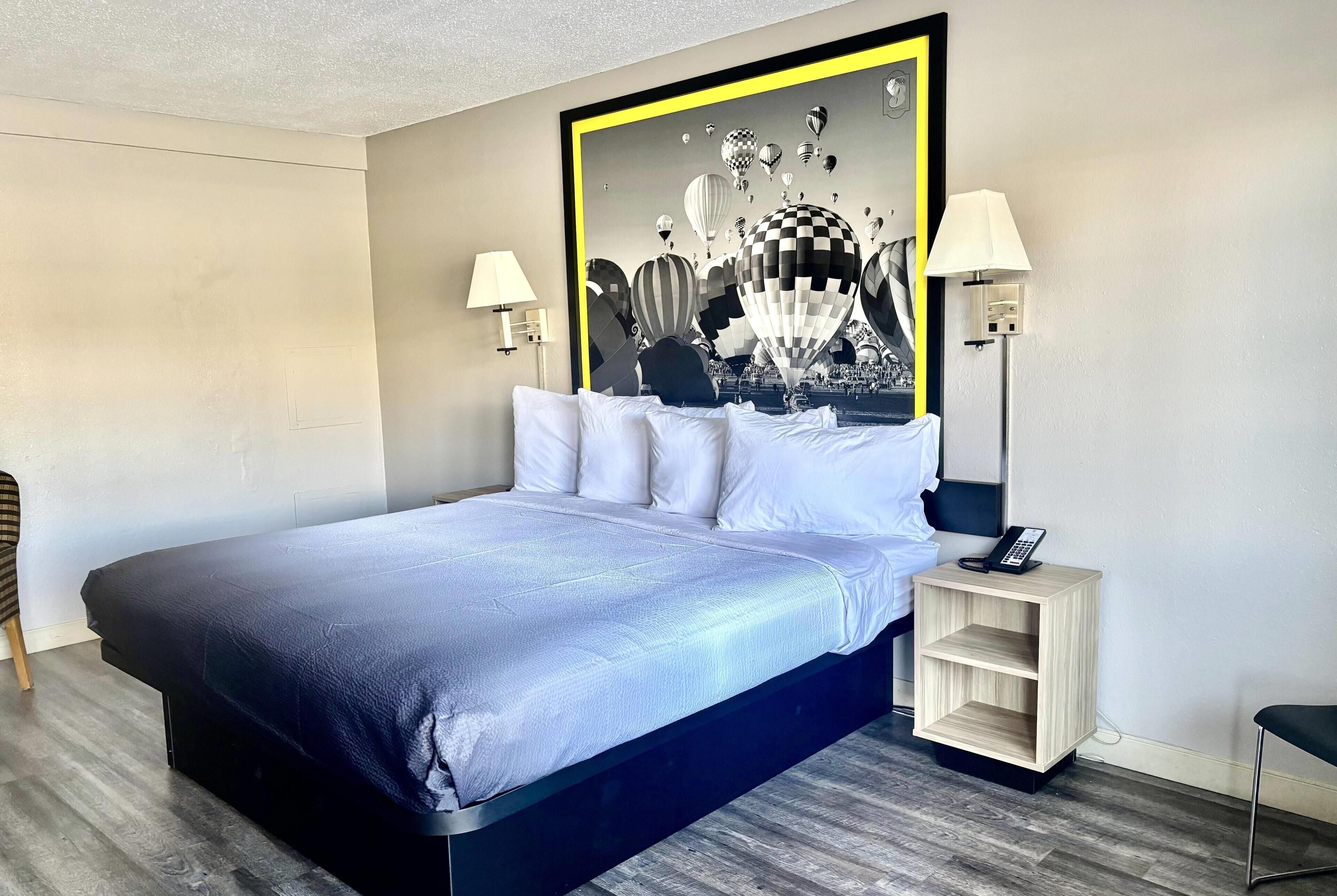 Una camera d'albergo con un letto, abat-jour, comodino e un quadro appeso al muro.