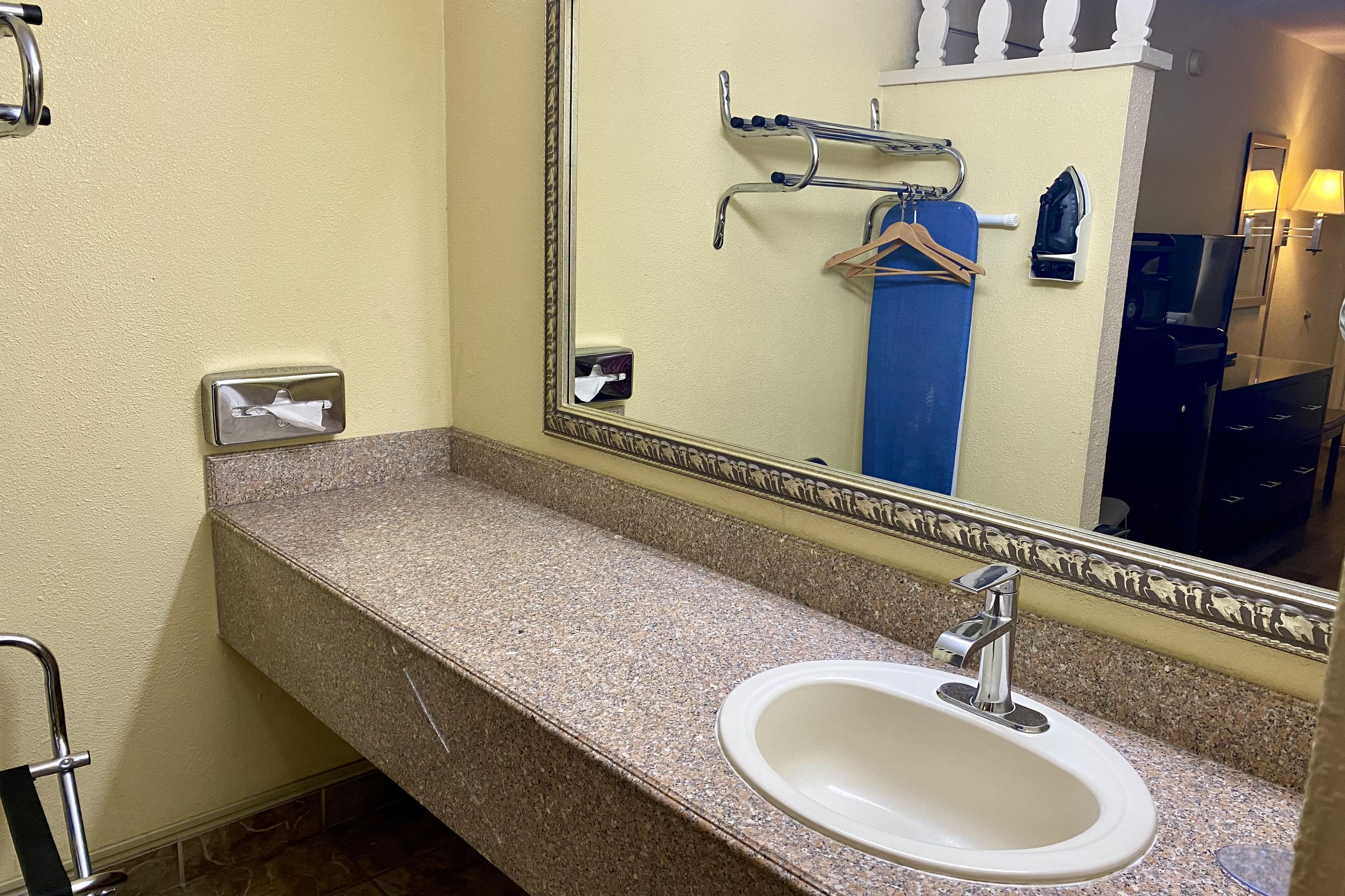 Un baño con encimera de granito, un lavabo blanco, un espejo con marco decorativo y un perchero con una toalla azul.