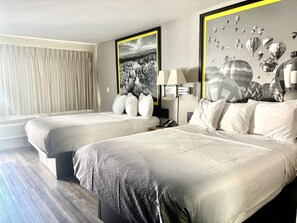 Una habitación de hotel con dos camas, un ventanal con cortinas y una pared decorada con cuadros.
