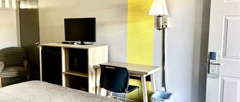 Une chambre d’hôtel comprenant un lit, un bureau avec une télévision, une chaise, une lampe et une poubelle.