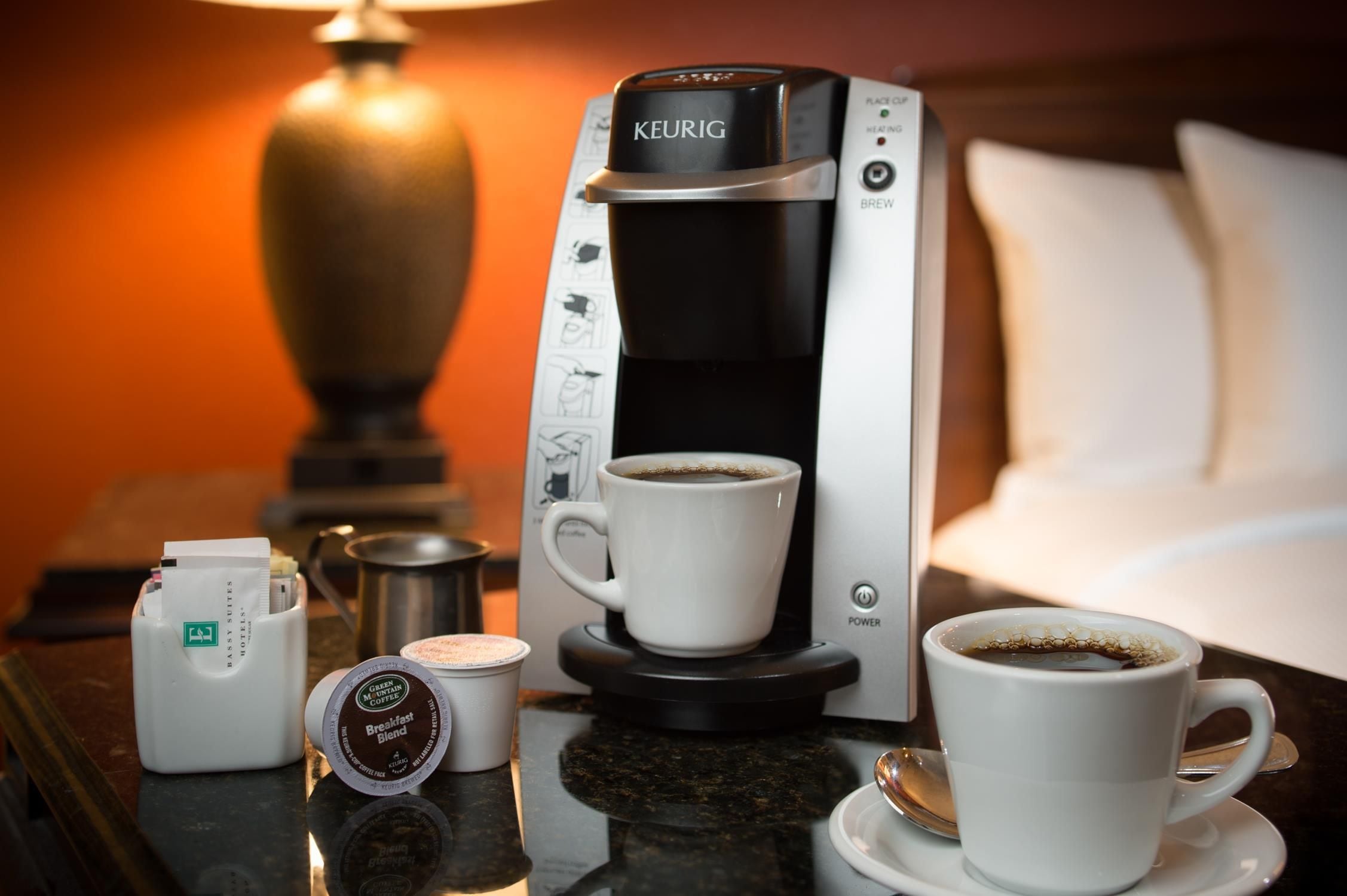 Une machine à café Keurig avec une tasse de café posée sur une table, une dosette Keurig de format voyage et une tasse Keurig de format voyage.