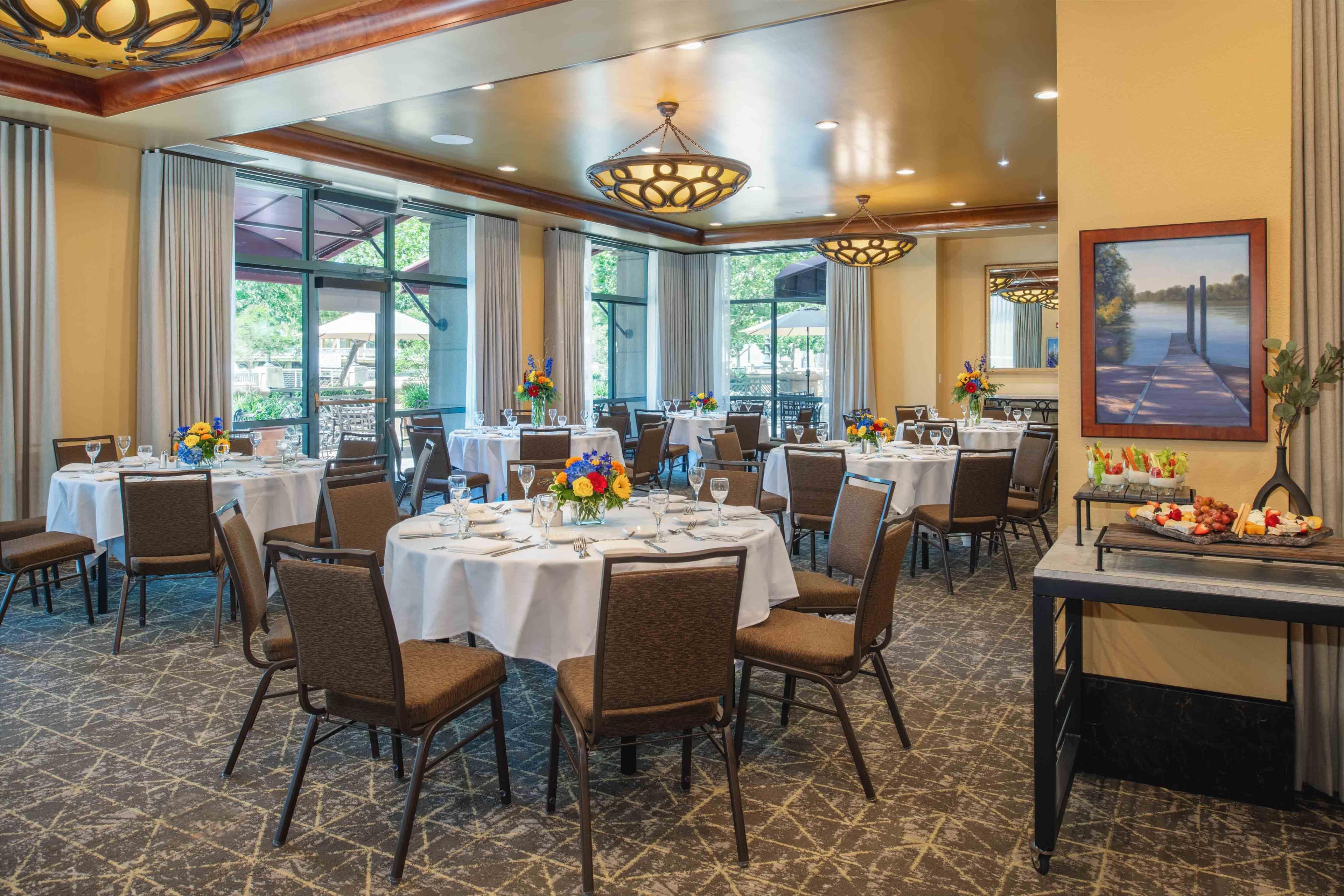 Une salle à manger d’hôtel avec plusieurs tables rondes, des chaises et une grande fenêtre donnant sur l’extérieur.