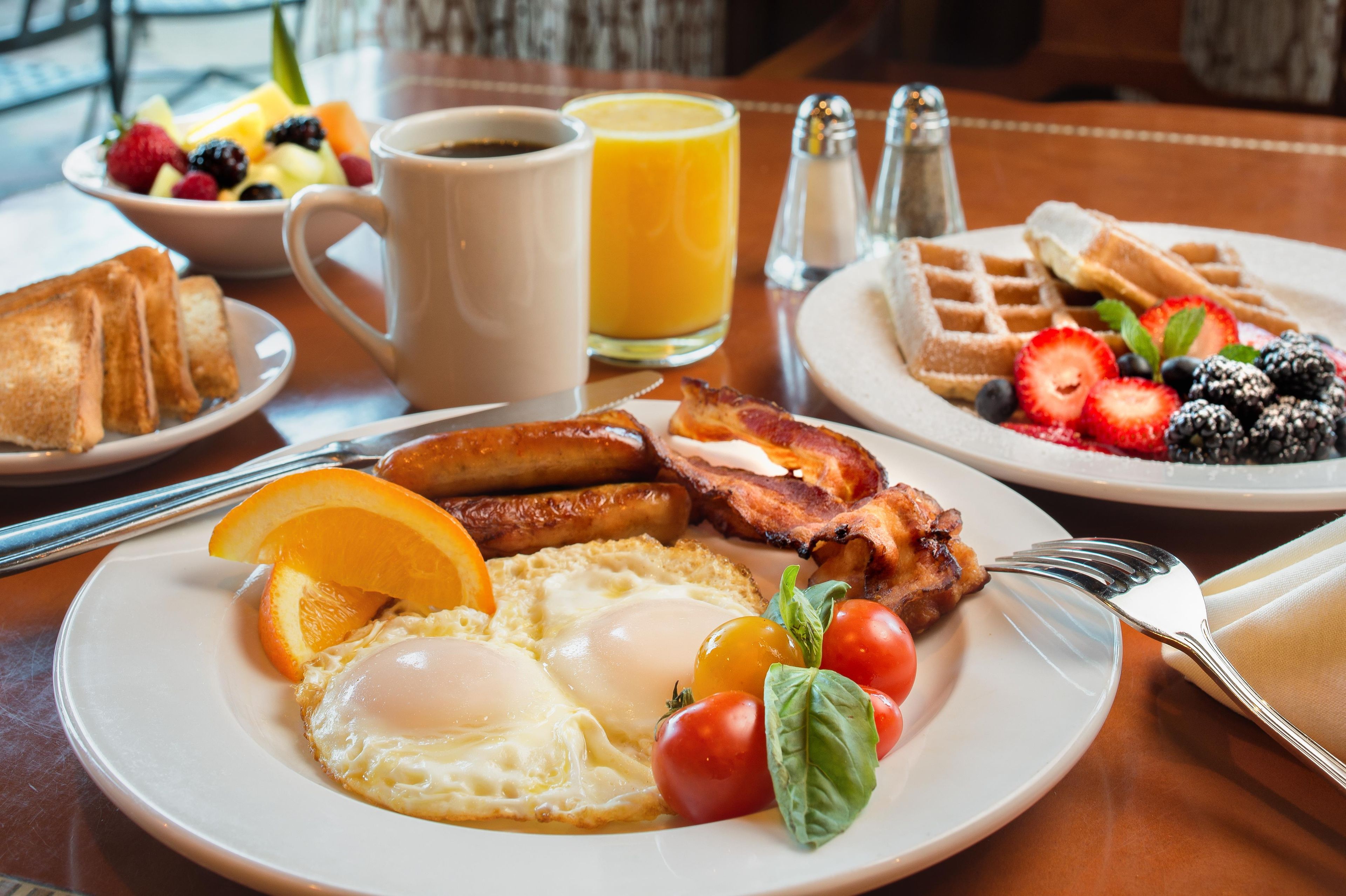 Une assiette de petit-déjeuner avec des œufs, du bacon, des tomates et une tranche d’orange.