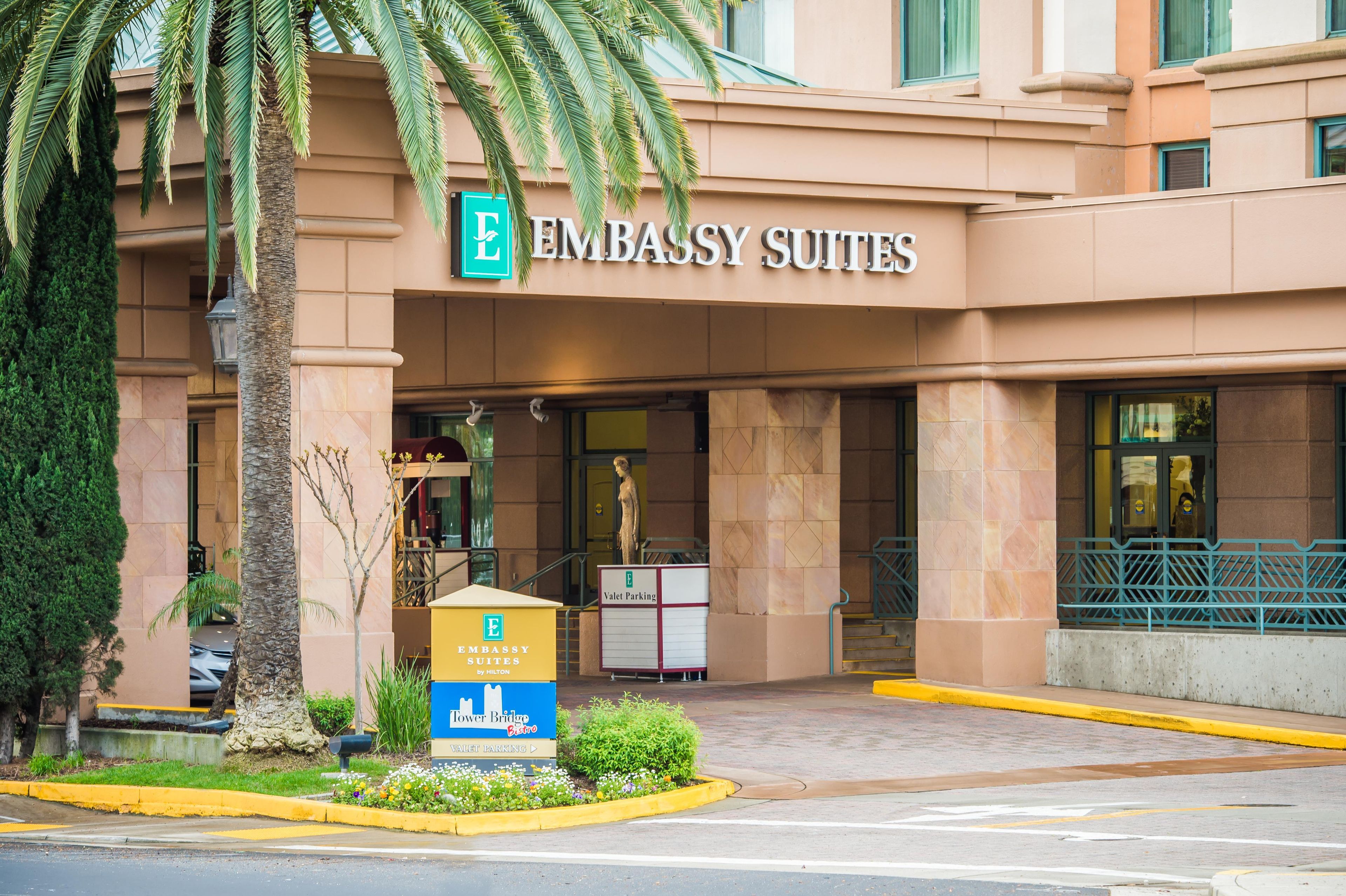 Außenansicht des Embassy Suites Hotels mit einem Schild für den Valet-Parkservice und einem nahegelegenen Restaurant.