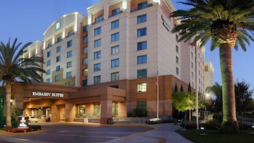 A multi-story hotel with 'EMBASSY SUITES' signage, a parking lot, and palm trees.