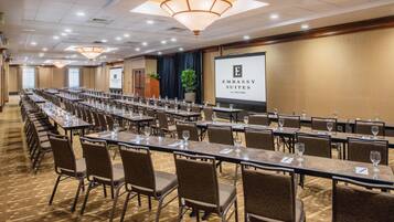 A conference room with long tables, chairs, and a projector screen displaying 'Embassy Suites by Hilton'.