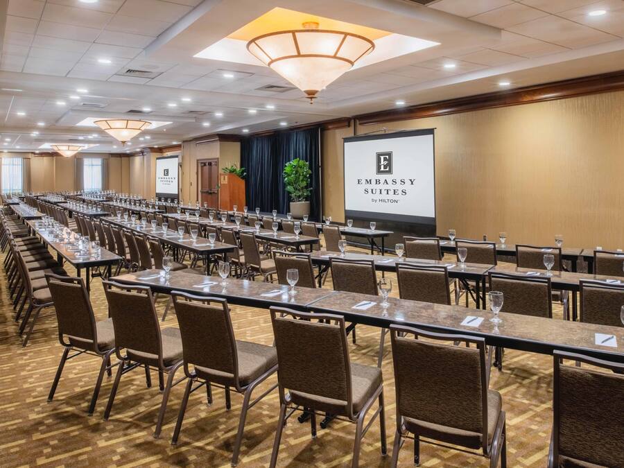 A conference room with long tables, chairs, and a projector screen displaying 'Embassy Suites by Hilton'.