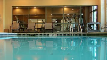 Piscina interna com vista clara para o ambiente adjacente, equipada com bicicletas ergométricas e cadeiras.