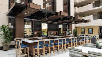 Una zona de bar con una barra alargada, distintas opciones de asientos y vistas al interior del edificio.