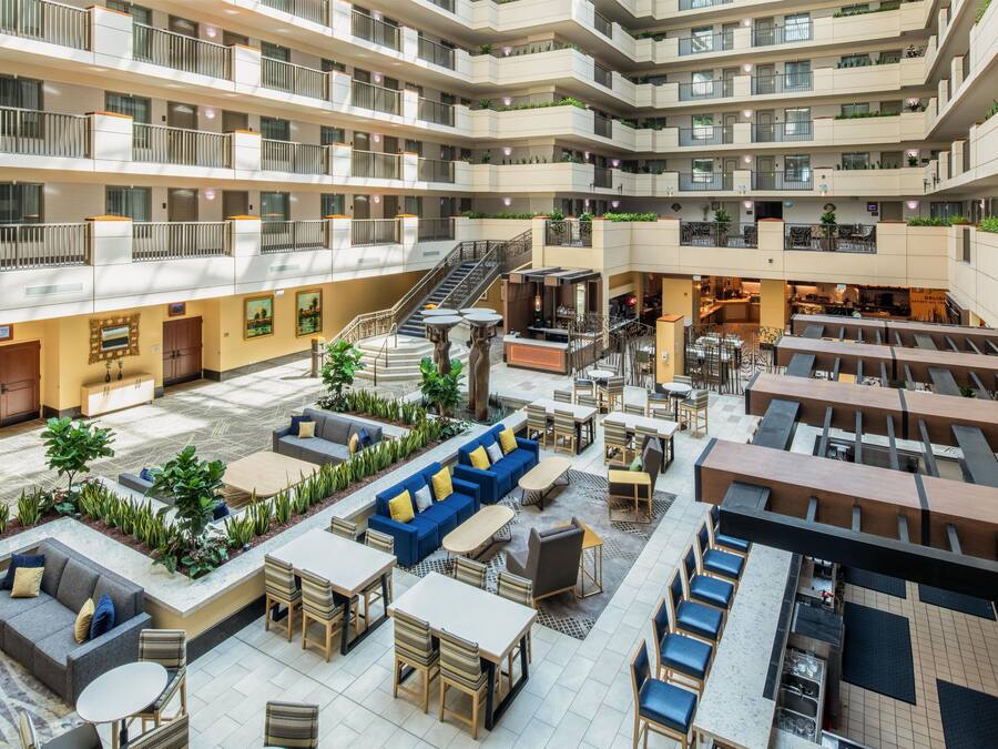 A multi-level hotel atrium with outdoor seating, a staircase, and a bar area.