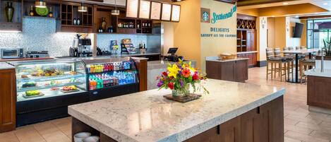 Un restaurante de hotel con una barra de mármol, una máquina de café, una pizarra de menú y un arreglo floral.