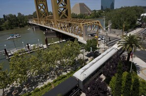 Spanning a river, a prominent bridge connects the city, with a tram line and lush greenery nearby.