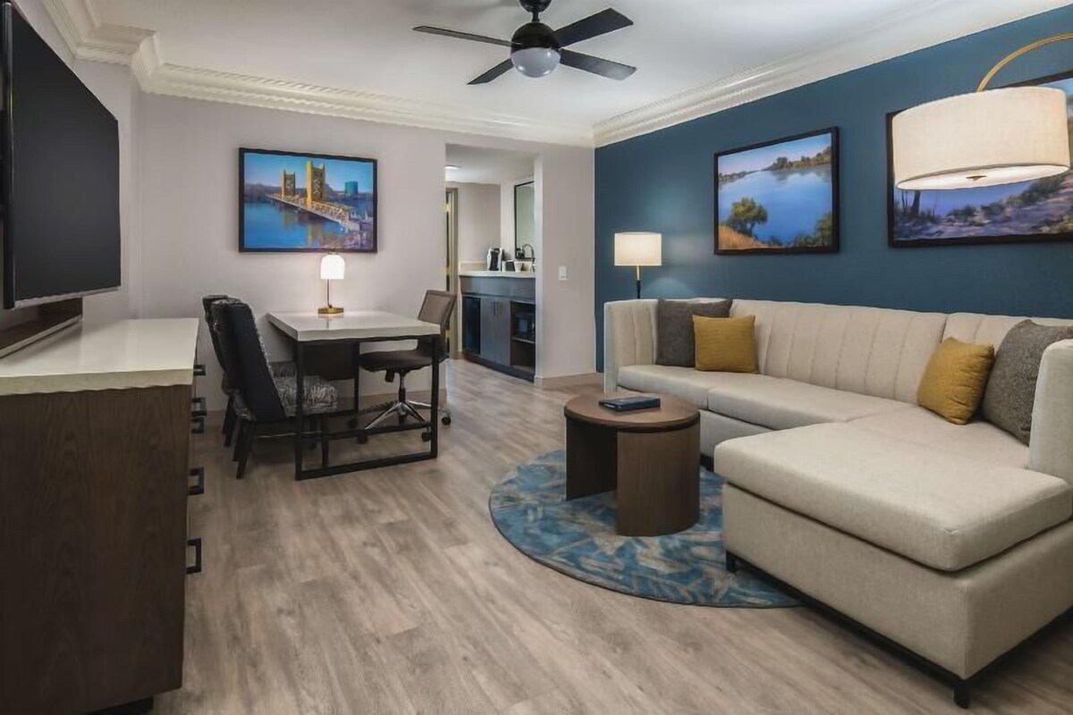 A hotel room with a dining area, a sofa, a TV, and artwork on the walls.