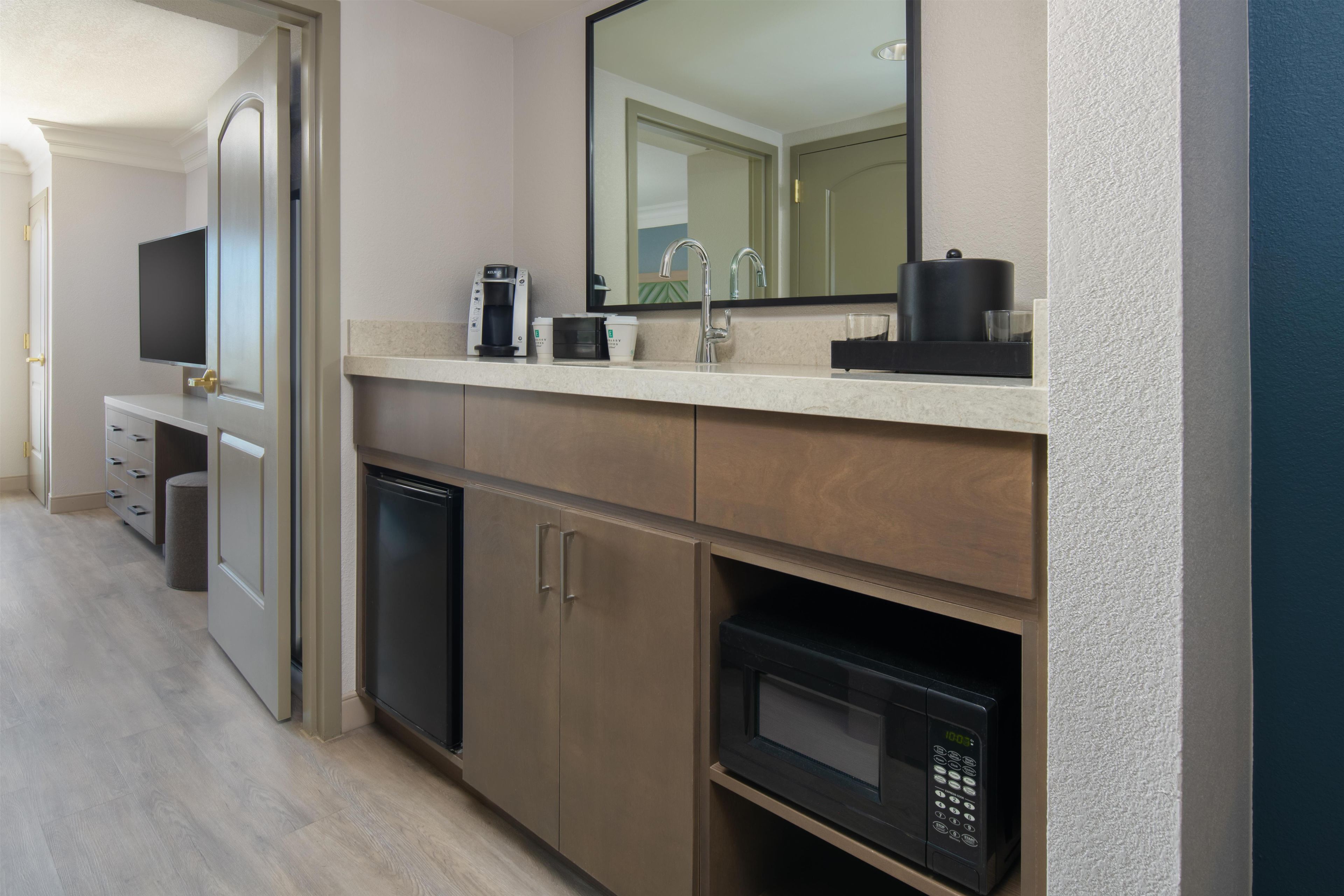 A modern kitchenette with a coffee maker, microwave, and a small refrigerator.