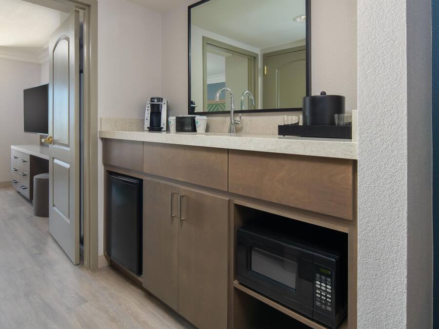 A modern kitchenette with a coffee maker, microwave, and a small refrigerator.