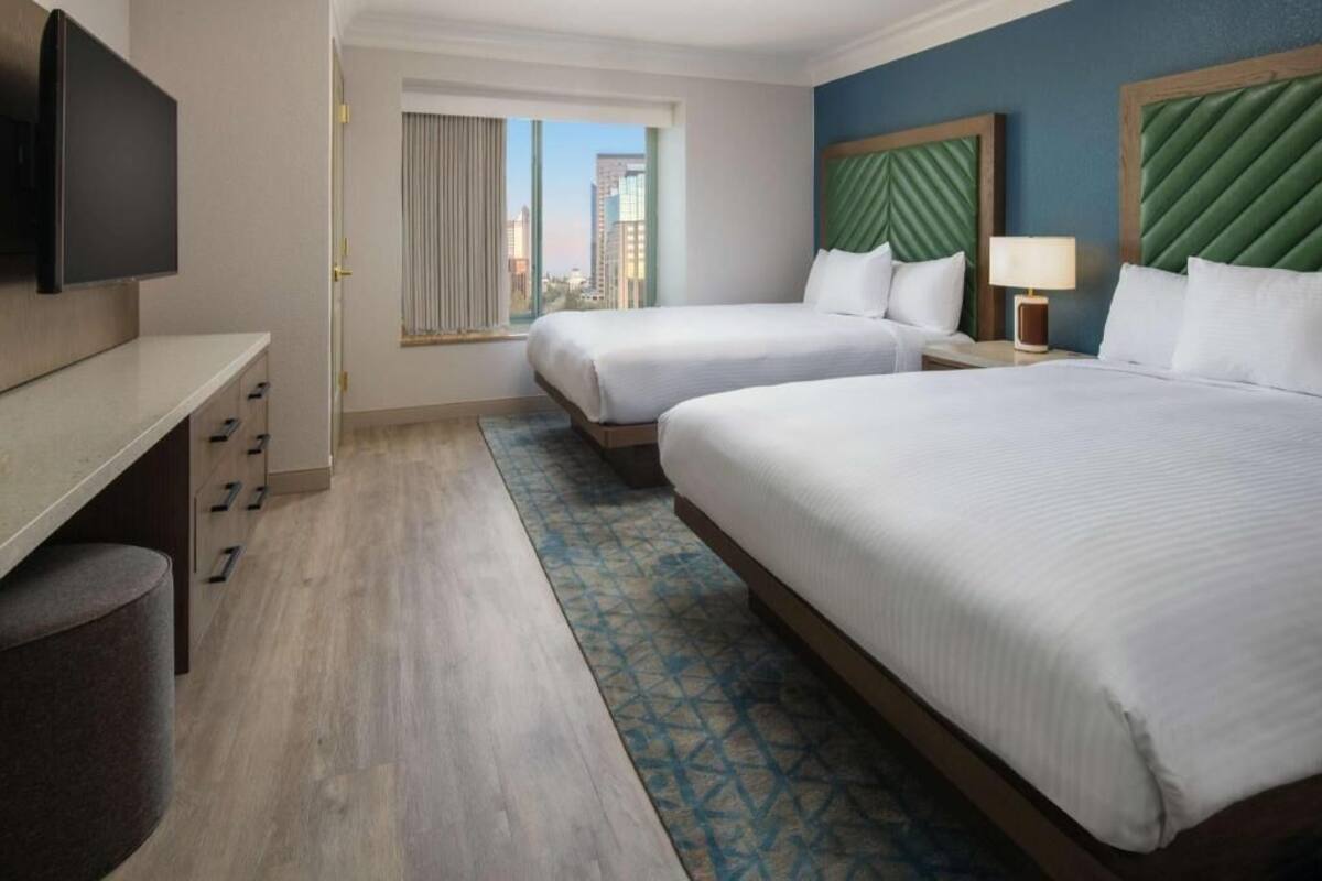 Habitación de hotel con dos camas, televisión, escritorio y vistas a la ciudad.