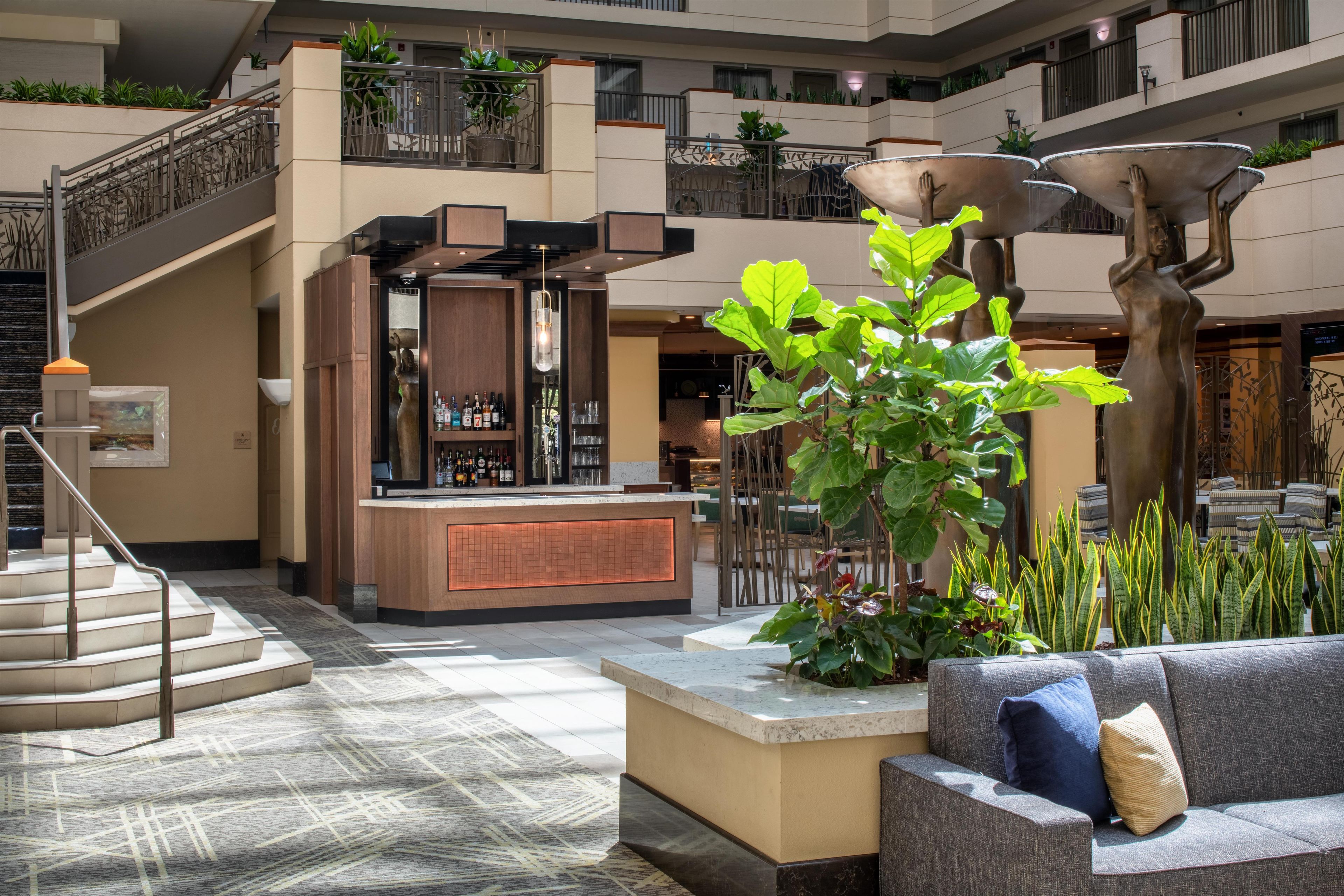 A spacious lobby with a central bar area, a staircase, and a seating area with a plant.