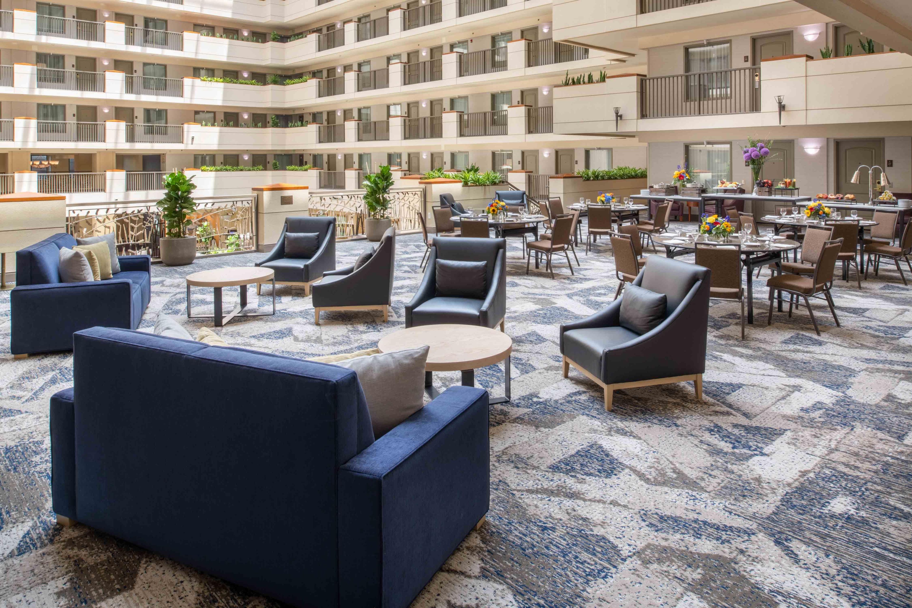 Eine großzügige Hotelhalle mit mehreren Sitzbereichen, darunter Sofas und Sessel, sowie ein Essbereich mit Tischen und Stühlen.