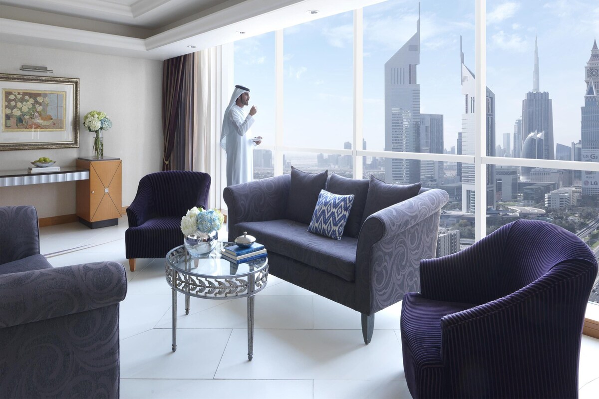 A modern living room with a city view, a sofa, armchairs, a glass coffee table, and a decorative vase.
