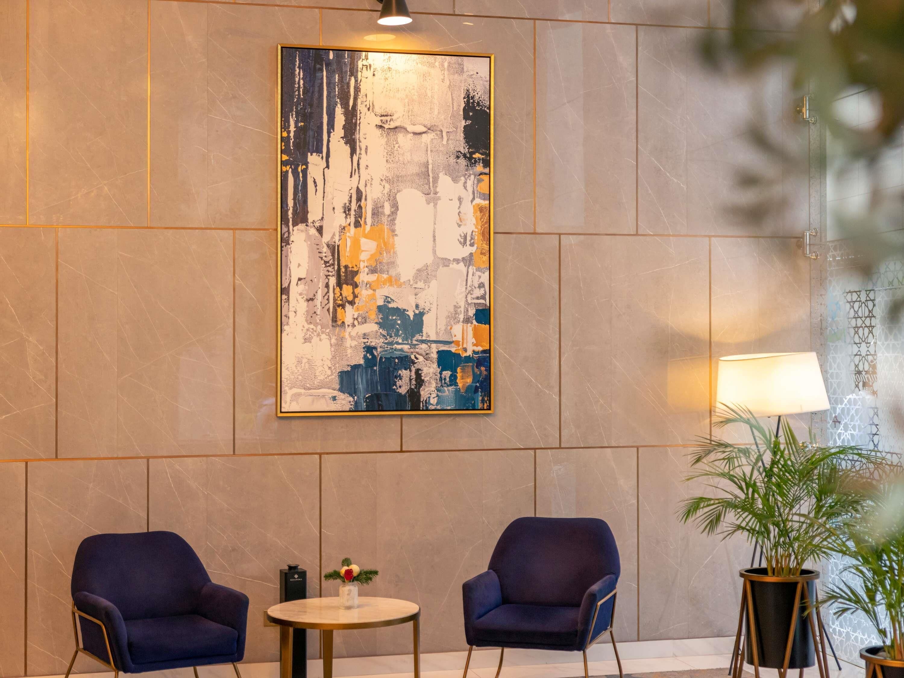 A lobby with two armchairs, a round table, a large abstract painting, and a potted plant.