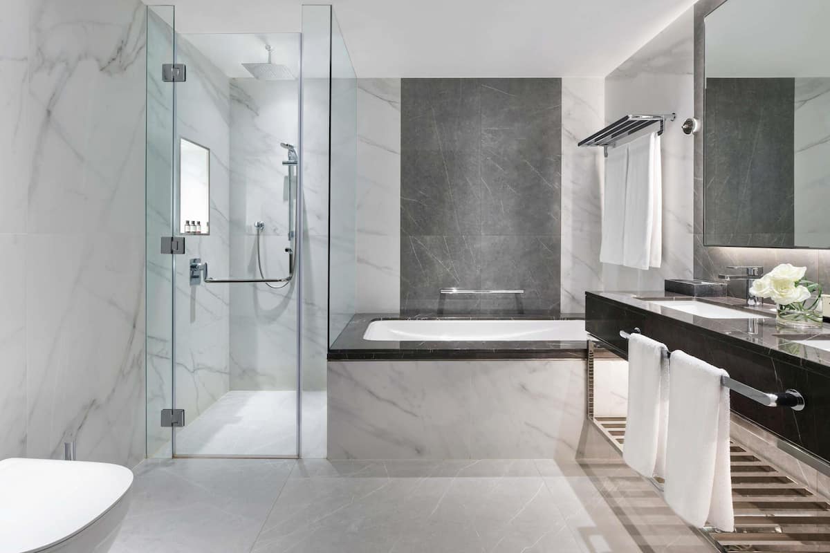 Ein modernes Badezimmer mit einer Duschkabine aus Glas, einer freistehenden Badewanne, einem großen Spiegel und einer dunklen Ablage mit Waschbecken und Waschtisch.