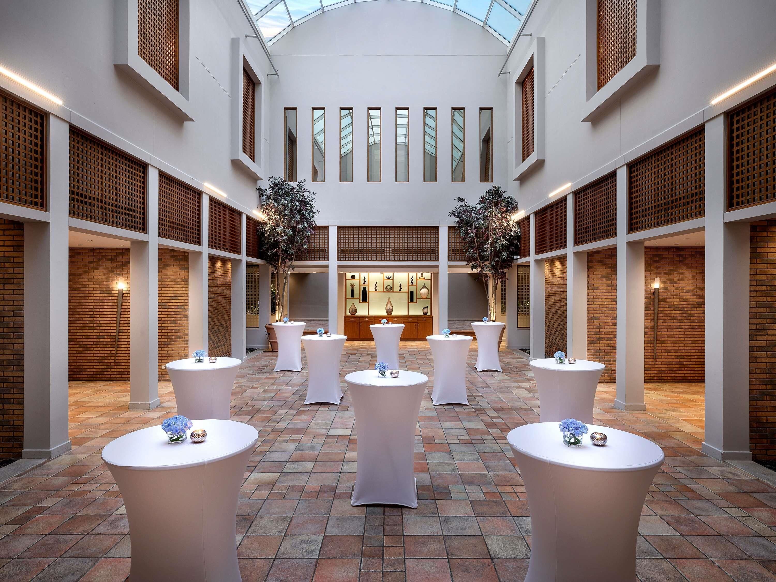 A spacious atrium with high ceilings, multiple tables, and potted plants.