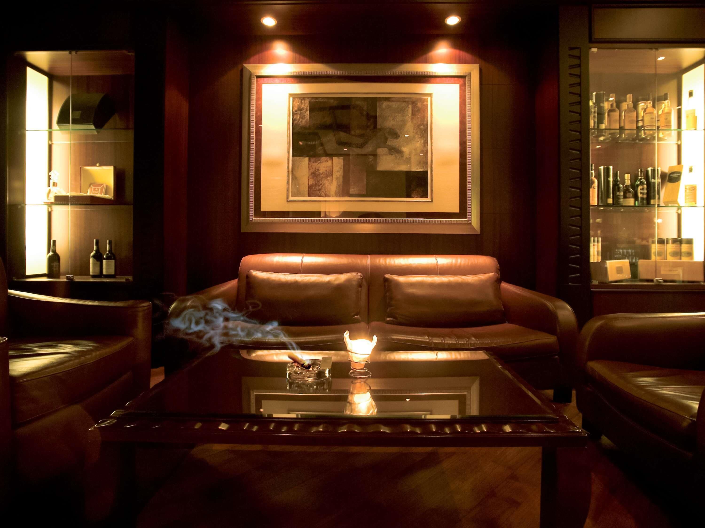 A dimly lit lounge area with leather seating, a glass table with a lit candle, and a framed artwork on the wall.