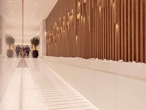 A modern hotel lobby with a reflective tiled floor, a wooden panel wall with recessed lighting, and a potted plant.