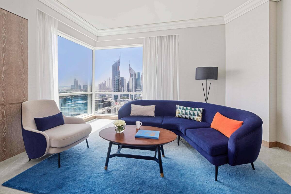 Ein modernes Wohnzimmer mit Blick auf die Stadt, ein blaues Sofa, ein beiger Sessel und ein runder Couchtisch.