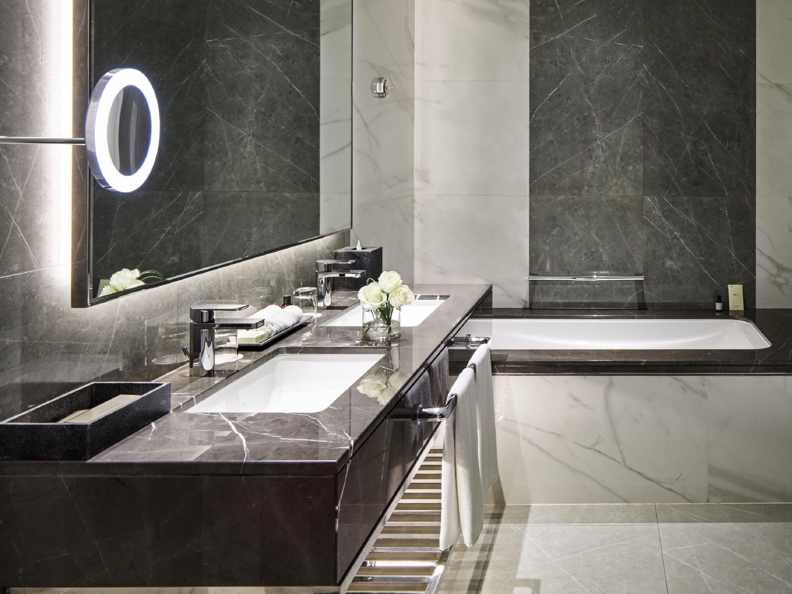 Un baño moderno con un espejo grande, dos lavamanos, una bañera y un tocador con encimera de mármol.