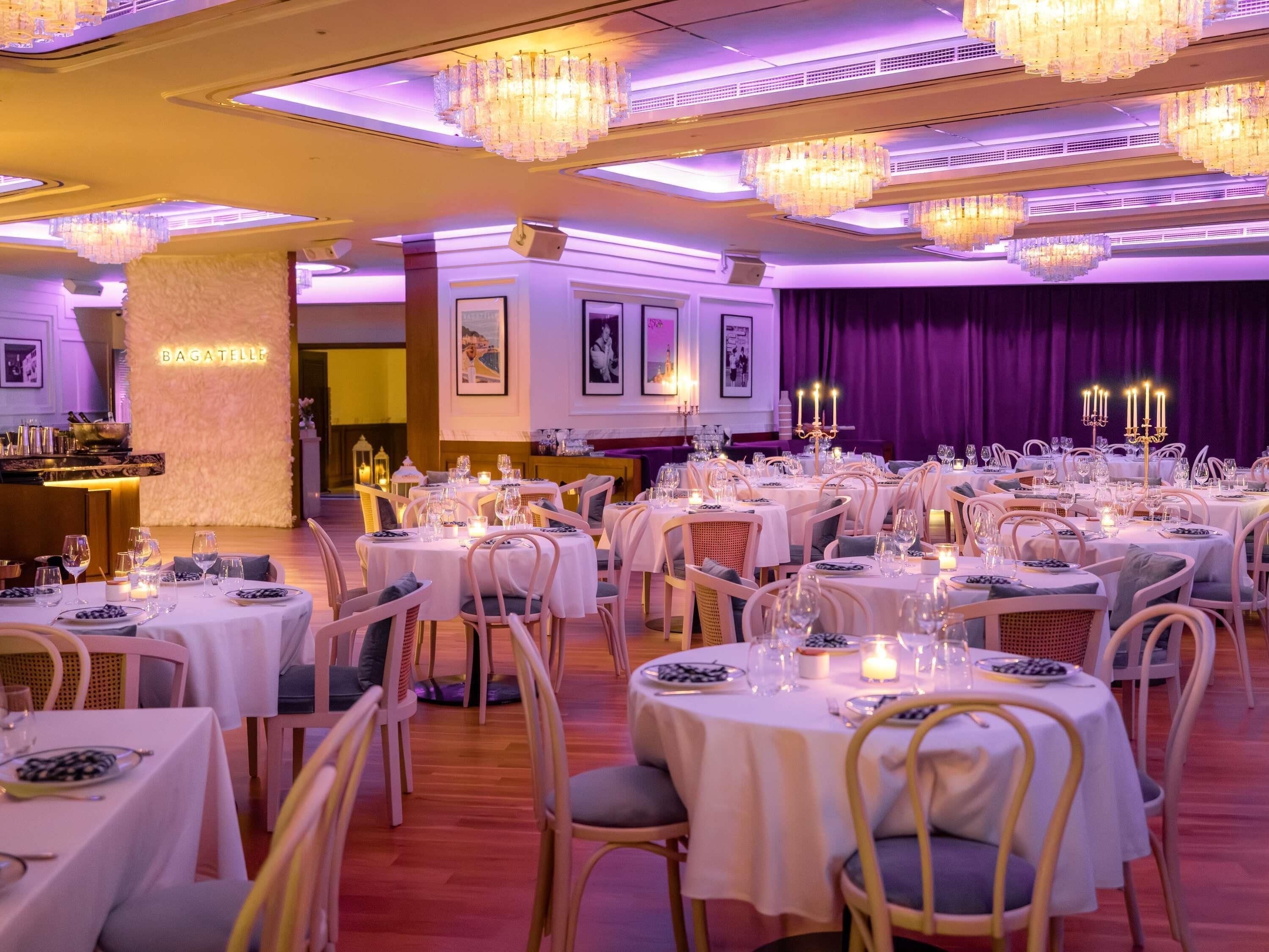 A restaurant with multiple round tables, white tablecloths, and candle centerpieces.