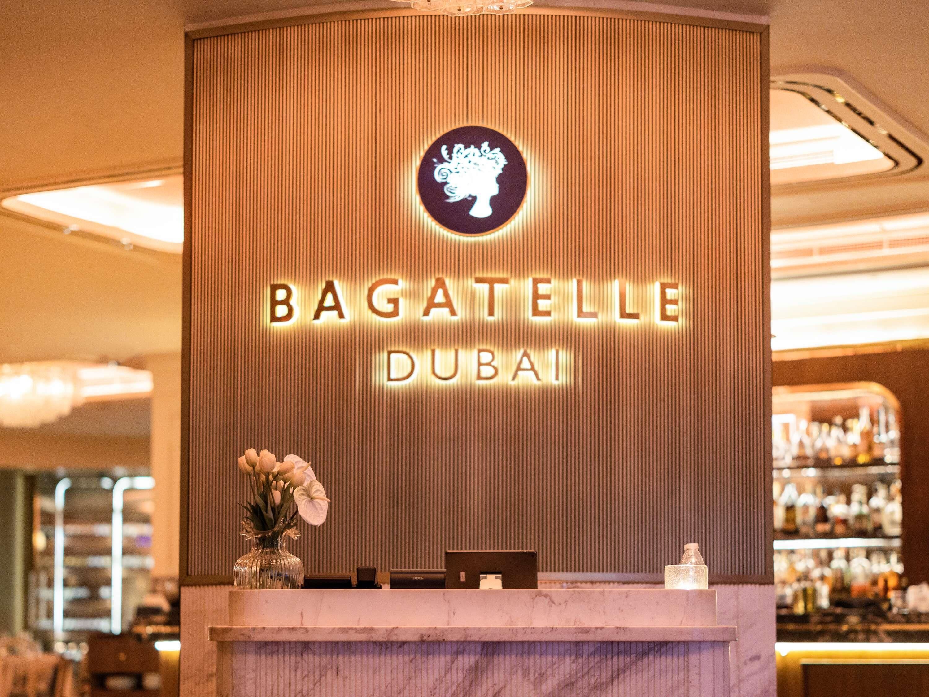 A reception desk with a sign reading 'BAGATELLE DUBAI' and a logo above it.