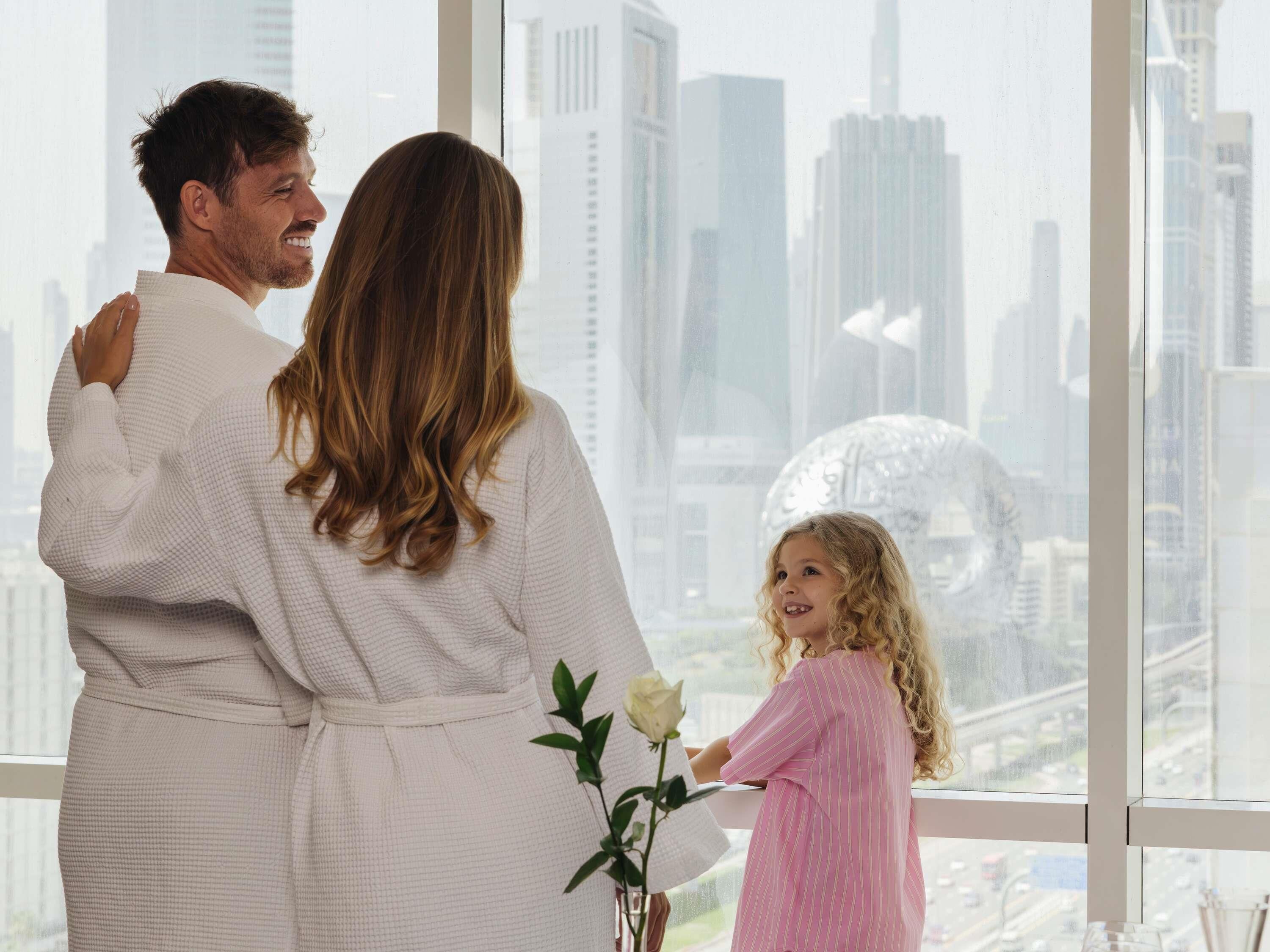 A family standing by a large window with a cityscape view.