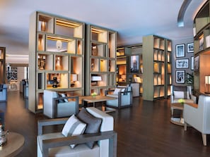 A modern hotel lobby with seating areas, wooden shelving with decorative items, and framed pictures on the walls.