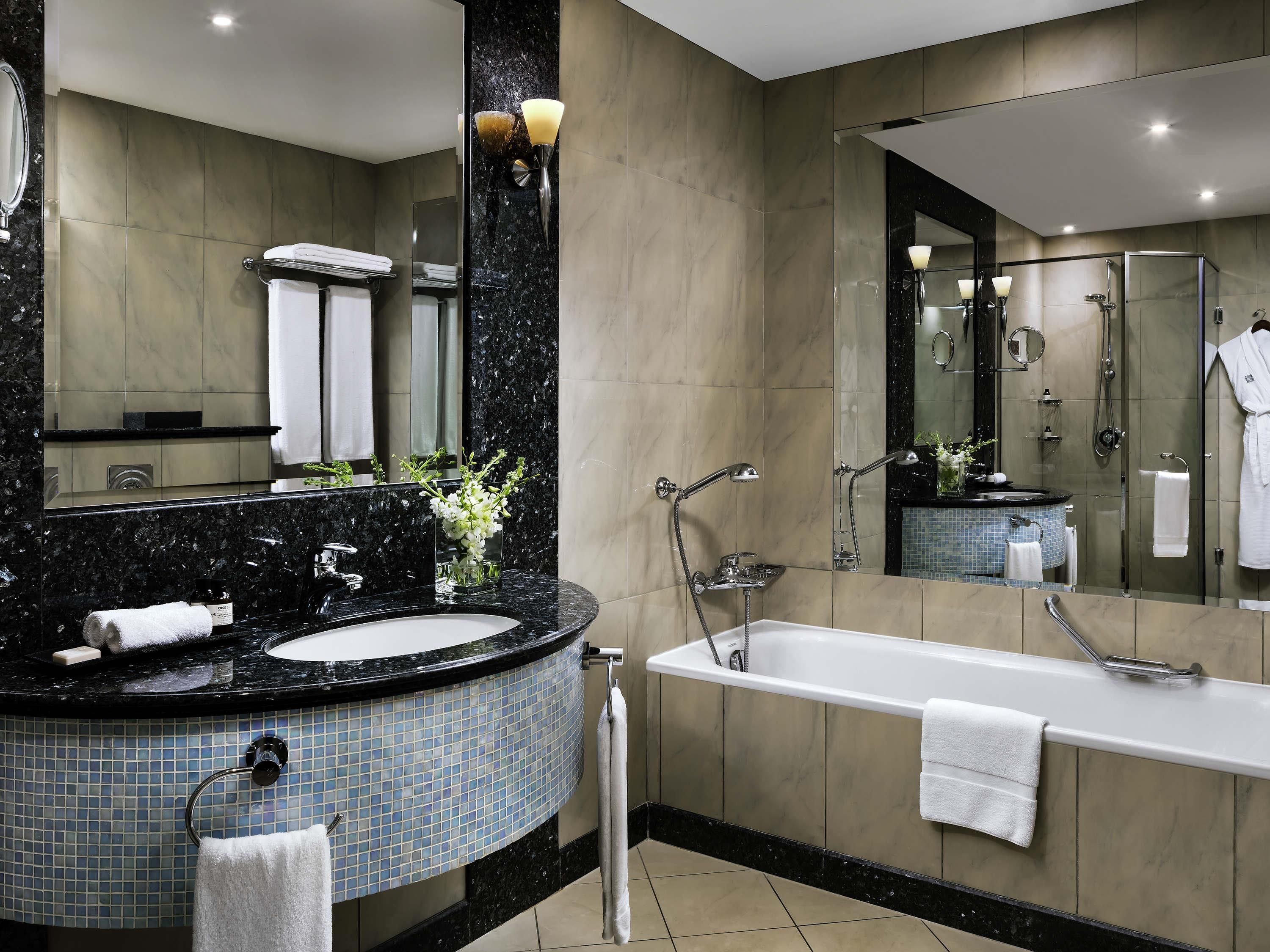 A modern bathroom with a black marble sink, a large mirror, a bathtub, and a glass-enclosed shower.