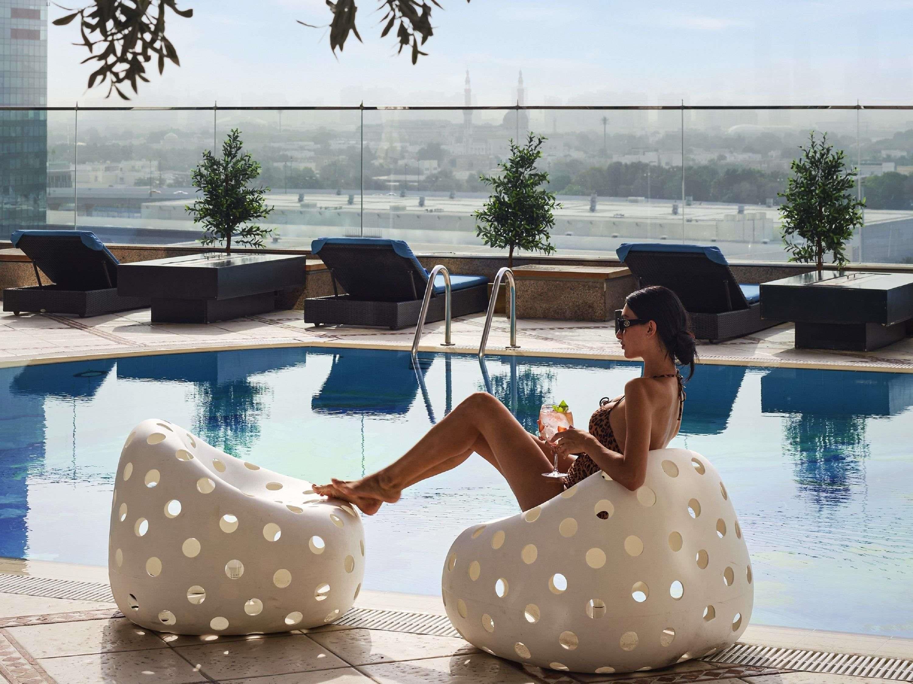 Un espace aménagé au bord de la piscine, avec des chaises longues, une piscine et une vue sur le paysage urbain.