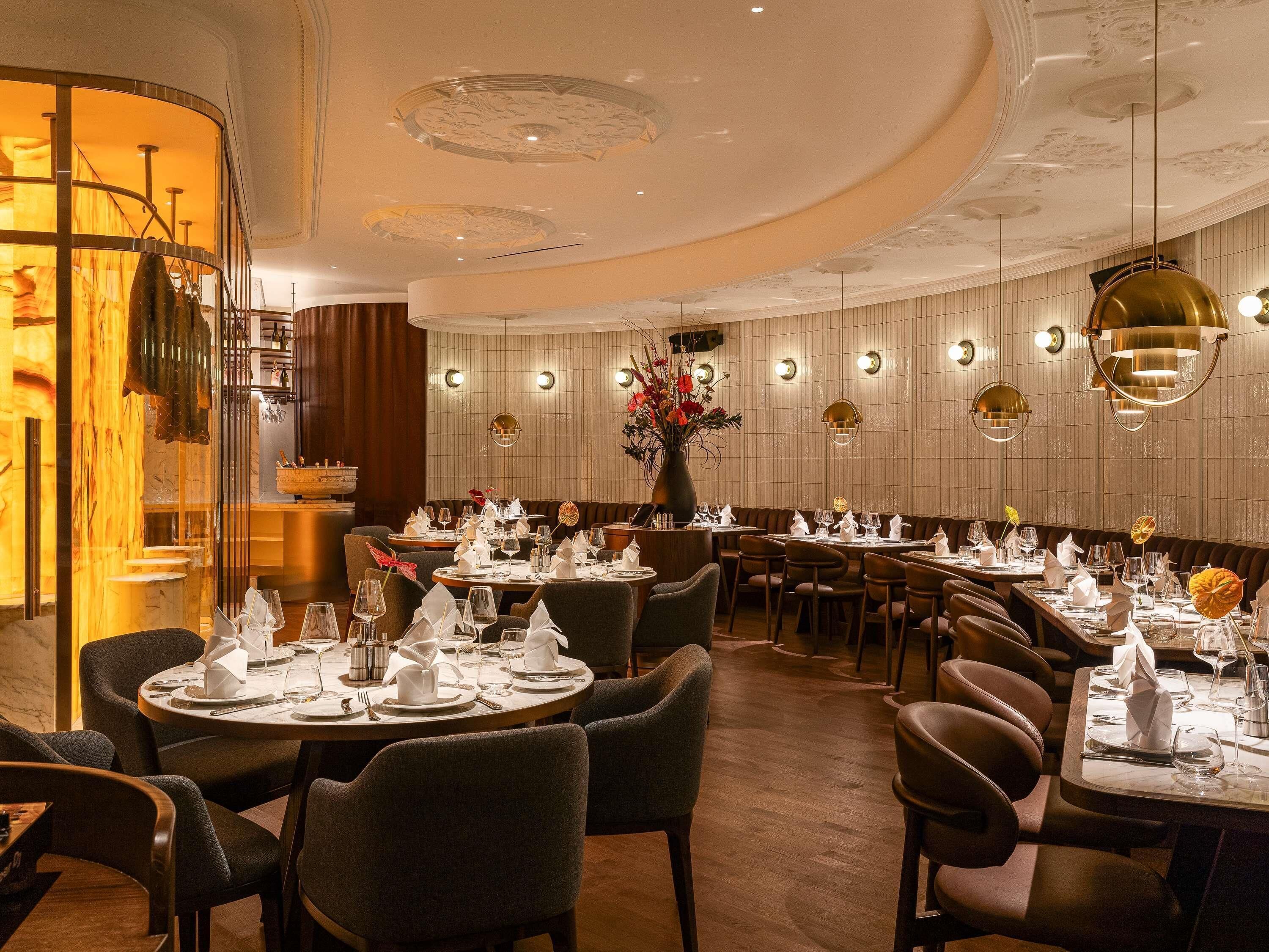 Un restaurante con mesas redondas, sillas oscuras y un arreglo floral central.
