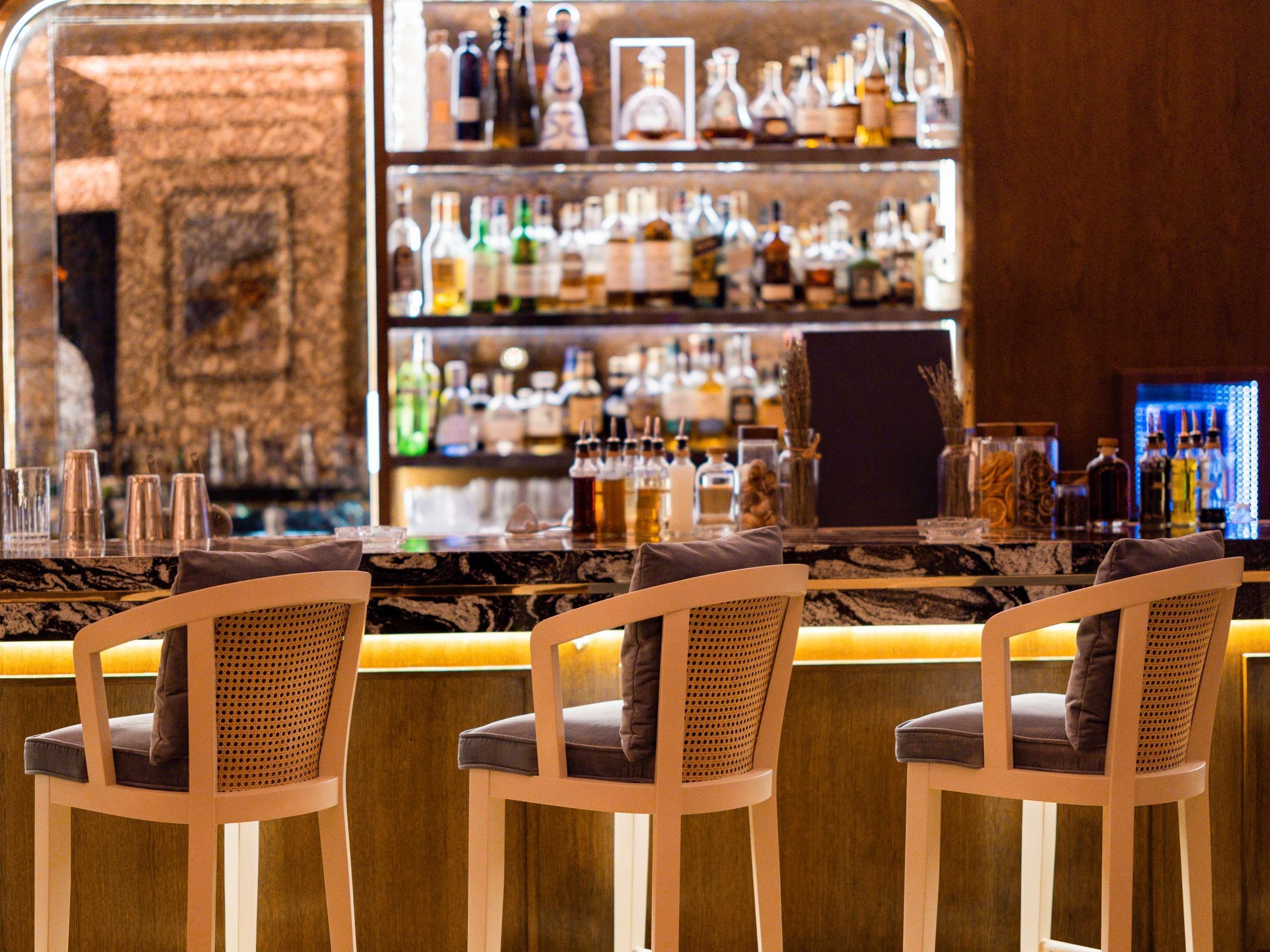 Eine Bar mit Marmorplatte, Korbstühlen und einer Auswahl an Flaschen und Gläsern.