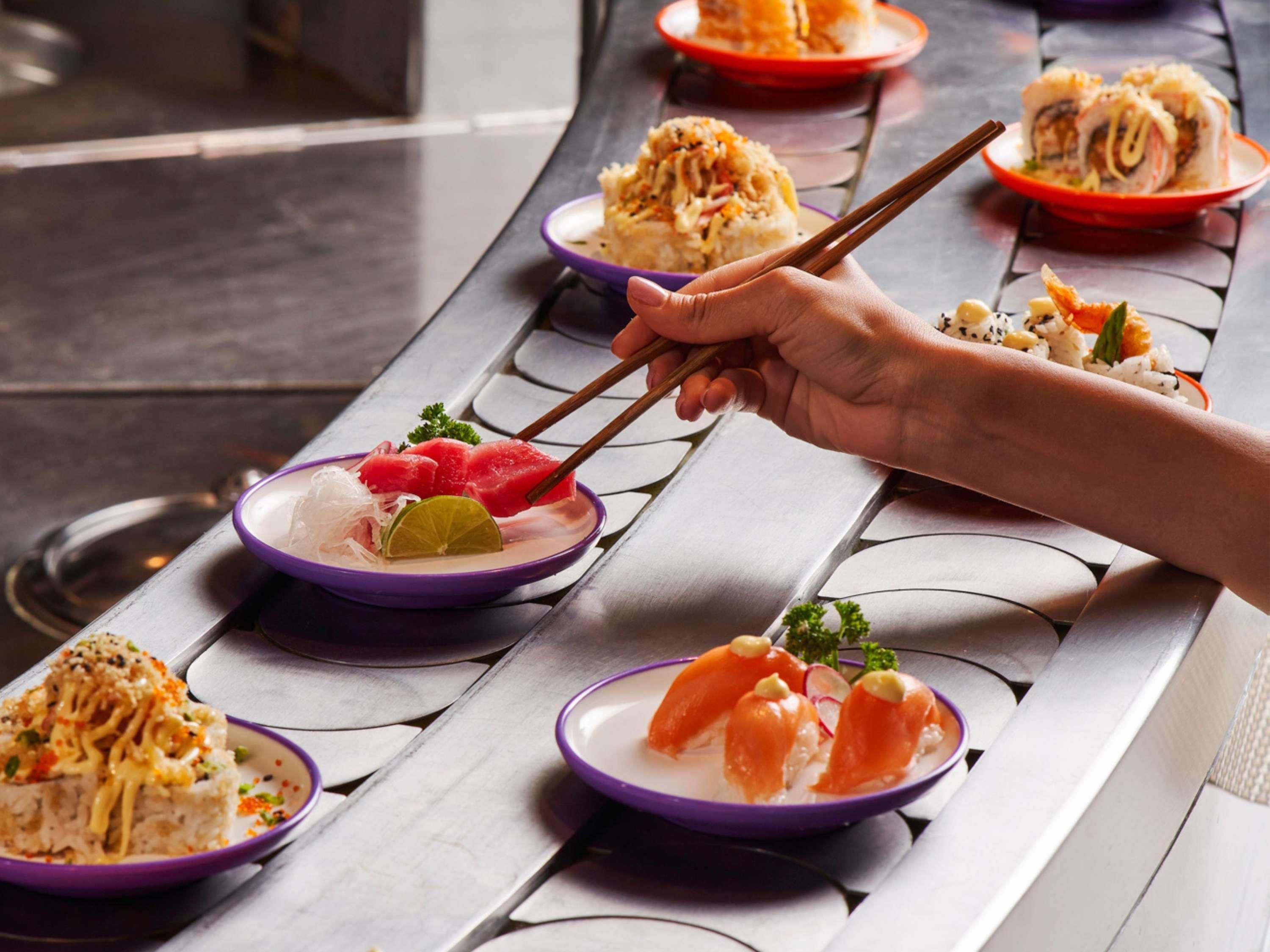 A dining table with various dishes, including sushi and rice, and a hand using chopsticks.