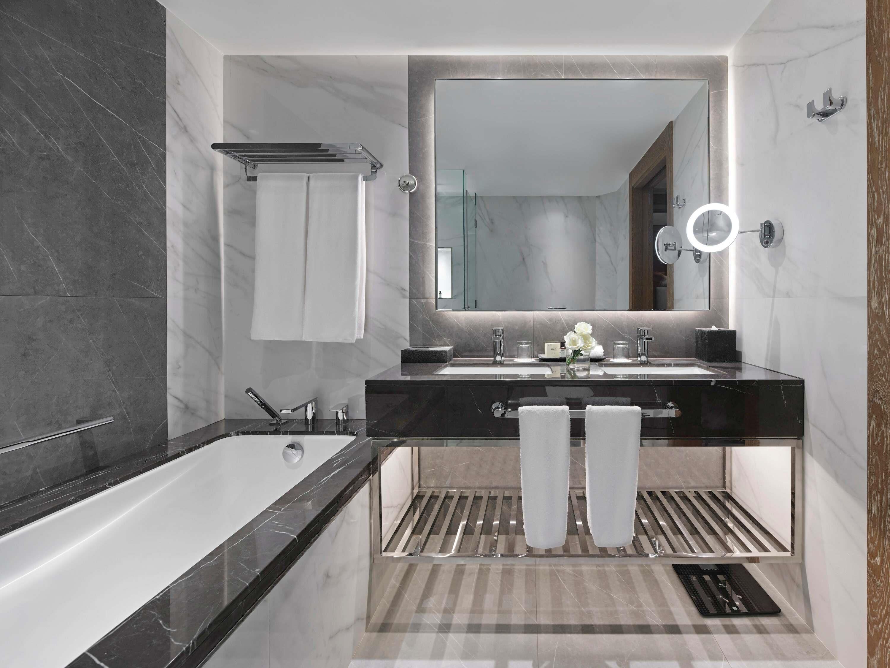 A modern bathroom with a large mirror, two sinks, a bathtub, and a towel rack.