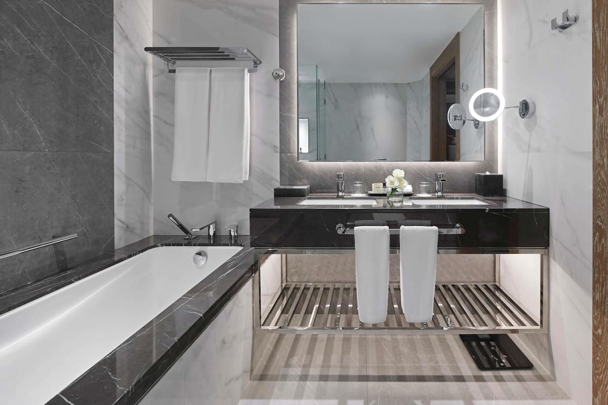 A modern bathroom with a large mirror, two sinks, a bathtub, and a towel rack.