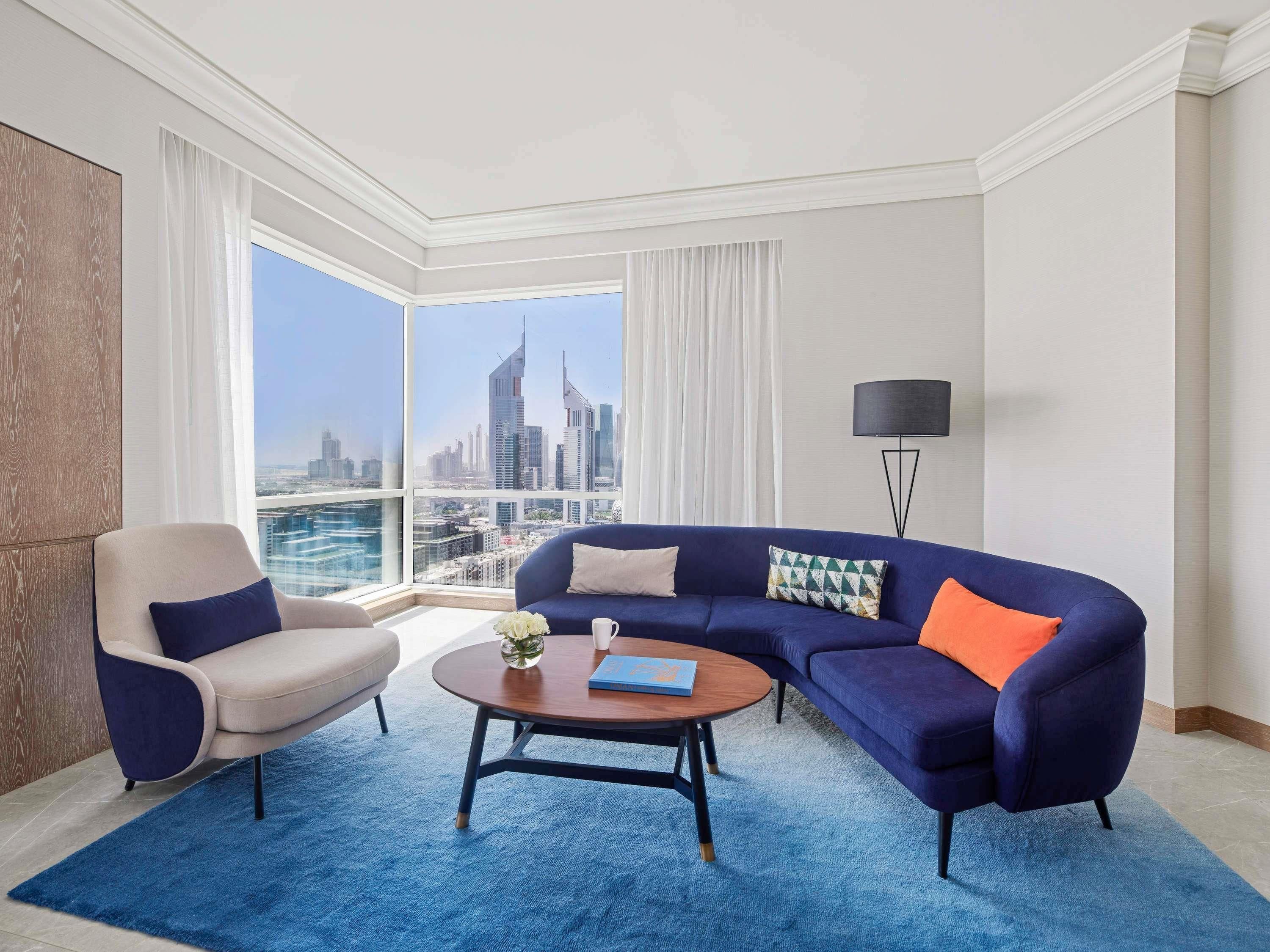 Un salon moderne avec vue sur la ville, un canapé bleu, une table basse ronde et une lampe.