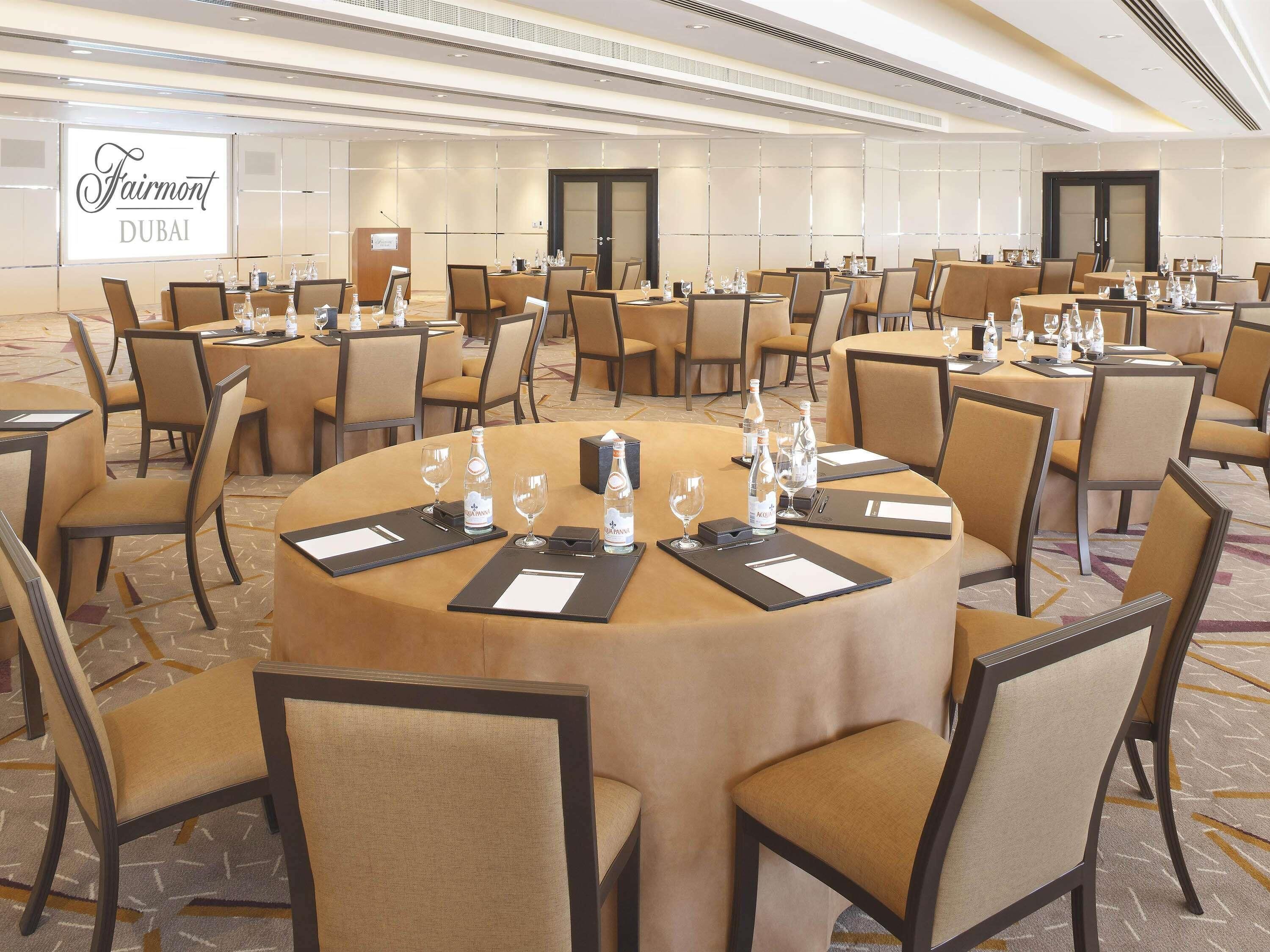 A conference room at Fairmont Dubai with round tables, chairs, and water bottles.