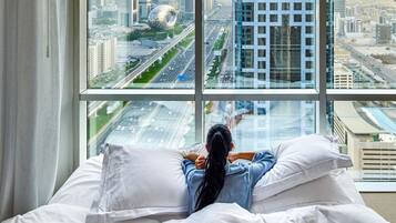 A person lying on a bed with a cityscape view through a large window.
