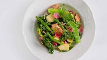 A white plate with a salad containing greens, potatoes, and salmon.